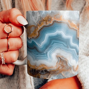 May include: A white ceramic mug with a blue and gold agate pattern. The mug has a handle and is perfect for coffee or tea.