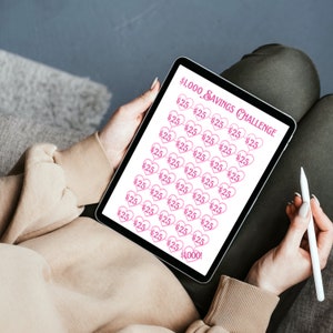 May include: A digital tablet displaying a savings challenge tracker with pink hearts and the text "£1,000 SAVINGS CHALLENGE". The tracker is divided into 40 sections, each with the number "£25" inside a heart. The last section reads "£1,000!"