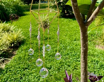 May include: A gold geometric planter with a small air plant inside. Five crystal prisms hang from the planter on gold chains.