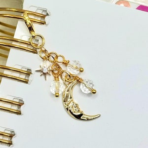 May include: Gold charm with a crescent moon, clear crystal beads, and a star charm. The charm is attached to a gold chain.