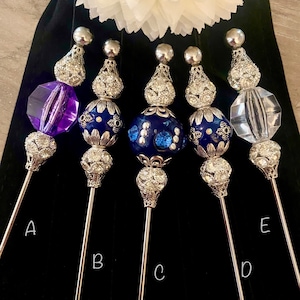 May include: Five decorative metal and glass bottle stoppers with blue and white accents. The stoppers are labeled A, B, C, D, and E.
