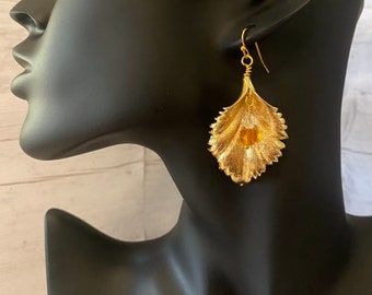 May include: Gold leaf earrings with a textured design and a dangling amber bead.