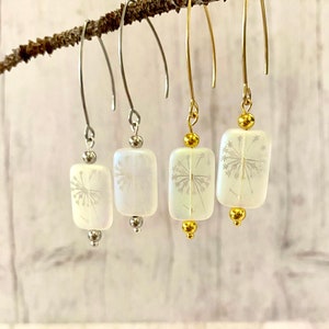 May include: Three pairs of dangle earrings with white rectangular glass beads featuring a pressed flower design. The earrings are available in silver and gold.