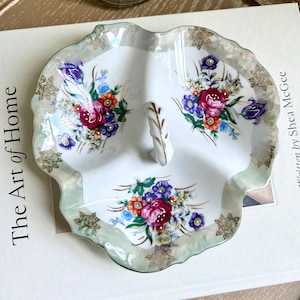 May include: A white porcelain serving dish with three sections, each decorated with a floral design in shades of pink, red, blue, and green. The dish has a gold rim and a scalloped edge.