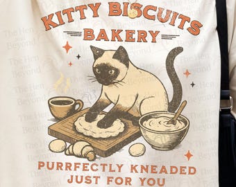 May include: A cream-colored t-shirt featuring a graphic of a Siamese cat kneading dough on a wooden board. The text reads KITTY BISCUITS BAKERY and PURRFECTLY KNEADED JUST FOR YOU. The design includes a coffee cup, a mixing bowl, and small stars.