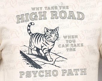 Könnte beinhalten: Cremefarbenes T-Shirt mit einer Schwarz-Weiß-Illustration einer Katze, die auf einer zerbrochenen Oberfläche geht. Der Text lautet: „WARUM DEN HIGH ROAD NEHMEN, WENN DU DEN PSYCHO PATH NEHMEN KANNST.“