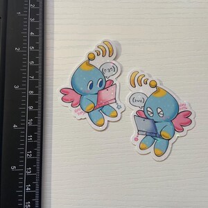 May include: Two stickers featuring a blue cartoon creature with a yellow head, pink wings, and holding a pink laptop. The stickers have a white border and the text "Nurse Kitty". The stickers are approximately 2 inches in height.