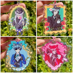 Puede incluir: Cuatro colgantes acrílicos con personajes de anime en marcos ornamentados. Cada colgante presenta un personaje diferente, con diferentes combinaciones de colores, incluyendo negro, azul, rojo y blanco. Los colgantes están sujetos a cuerdas rojas o rosas.