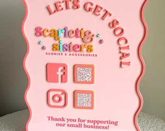 May include: A light pink wavy-edged sign featuring the text LETS GET SOCIAL, scarlette & sisters, SUNNIES & ACCESSORIES, and Thank you for supporting our small business. It includes Facebook and Instagram icons with two corresponding QR codes.