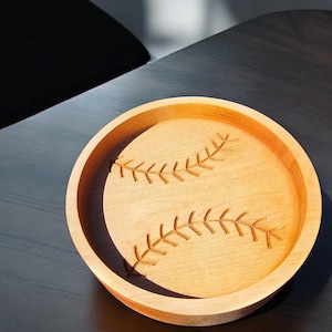 Puede incluir: Un tazón de madera con forma de pelota de béisbol con costuras cosidas talladas en la superficie.
