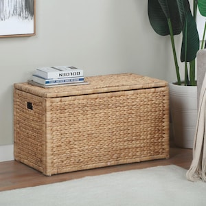 May include: A rectangular woven storage trunk in a natural tan color. The trunk has a hinged lid and a rectangular handle on the front. Two books are stacked on top of the trunk. The text on the books reads "GOLDEN" and "THAT JUSTICE SHALL BE DONE".