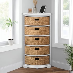 May include: A white corner storage cabinet with five woven wicker drawers. The cabinet has a curved front and is placed near a window. A small plant and decorative items sit on top.