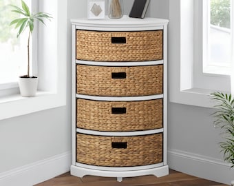 May include: A white corner cabinet with four woven wicker drawers. The cabinet is in a bright room with a window and a potted plant. The drawers have rectangular handles.