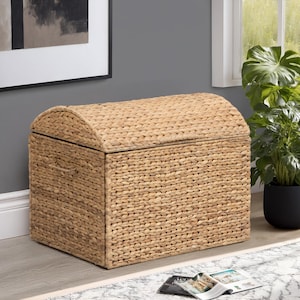 May include: A woven storage chest with a domed lid. The chest is made of natural-colored woven material. The chest is rectangular with a curved top. The chest is sitting on a light-colored floor.