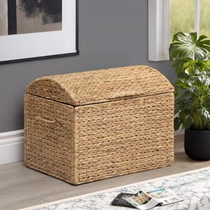 May include: A woven storage chest with a domed lid. The chest is made of natural-colored woven material and has a rectangular shape with a curved top. It features a handle on the side and is suitable for storing items.