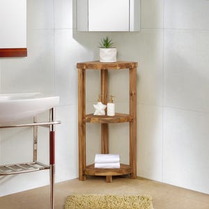 May include: A three-tiered, corner bathroom shelf made of light brown wood. The shelf holds a small potted plant, two soap dispensers, and a stack of white towels. The shelf is placed in a bathroom with white tile walls.