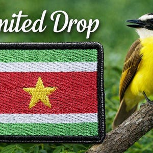 May include: A rectangular embroidered patch featuring the flag of Suriname with horizontal green, white, and red stripes and a central yellow star, accompanied by a yellow and brown bird perched on a branch with the text Limited Drop above.