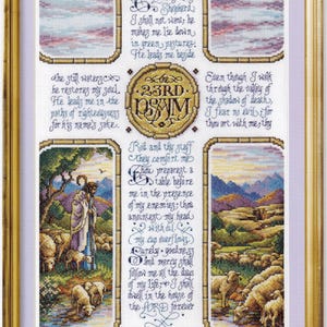 Op de afbeelding: Een ingelijst kruissteek borduurwerk met Psalm 23 in donkerblauwe kalligrafie. Het ontwerp bevat vier rechthoekige landschapsscènes met schapen en een herder, gevat in een goudkleurige lijst met een lichtpaarse passe-partout rand.