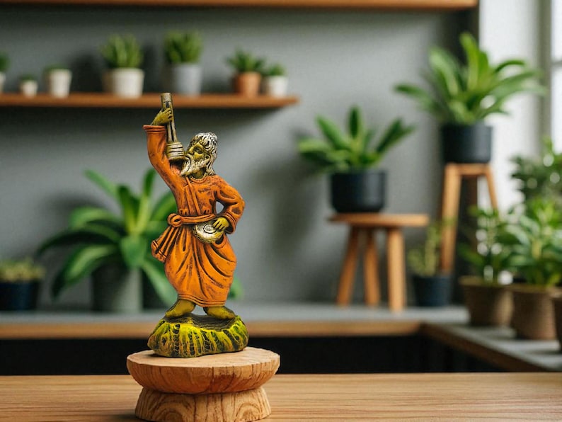 Handcrafted terracotta Baul musician statue with ektara displayed on a wooden pedestal, surrounded by indoor potted plants in a modern green-themed interior.
