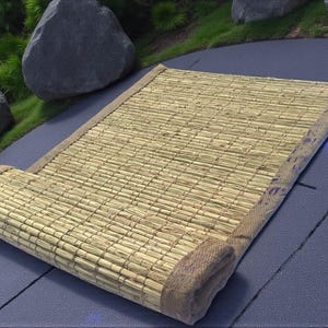 May include: A partially rolled rectangular mat made from woven natural fibres, possibly bamboo or straw. It has a tan border. The background features rocks and greenery. The mat's dimensions are approximately 180 cm long.