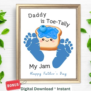 May include: Framed print with a gold border featuring a cartoon image of toast with jam and a blueberry, blue footprints, and the text "Daddy is Toe-Tally My Jam Happy Father's Day". Includes a "BONUS" tag.