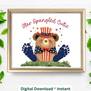 May include: A framed print featuring a watercolor illustration of a brown bear wearing a patriotic hat, cape, and bow tie. The bear has blue footprint-shaped feet and is sitting on grass. The text "Star Spangled Cutie" is written above the bear.