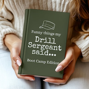 May include: A hardcover book with a dark green cover, held by a person. The book's cover features the text "Funny things my Drill Sergeant said... Boot Camp Edition" in white, along with a line drawing of a military cap.