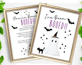 May include: Two printable Halloween "Booed!" signs with a ghost and a black cat. The signs are in gold frames and have a white background with black text. The text on the signs reads "You've Been Booed!" and "I've Been Booed!"