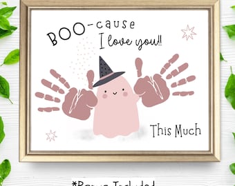 Puede incluir: Una impresión enmarcada con borde dorado presenta un fantasma rosa con un sombrero de bruja, con arte de huellas de manos. El texto dice "BOO-cause I love you!! This Much" con acentos de estrellas. La frase "*Bonus Included" está en la parte inferior.