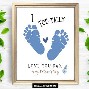 May include: Framed print with the text "I TOE-TALLY LOVE YOU DAD! Happy Father's Day" and blue footprints. The print has a gold frame and is decorated with green leaves.