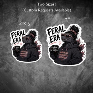 Op de afbeelding: Twee stickers met een Godzilla-achtig wezen met een zonnebril en een hoodie, met een koffiemok. De stickers lezen "FERAL ERA" en "UNBOTHERED UNAPOLOGETIC UNSTOPPABLE". Verkrijgbaar in 5.08 cm x 12.7 cm en 7.62 cm.