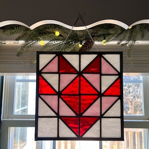 May include: A stained glass window panel featuring a red heart design with pink and white accents. The heart is made up of geometric shapes and is framed in black.