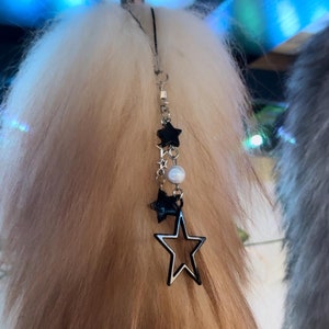 May include: A fluffy, ombre-colored tail with a silver chain and star charms. The tail transitions from white to light brown. The chain features black star charms, a pearl-like bead, and a silver star pendant.