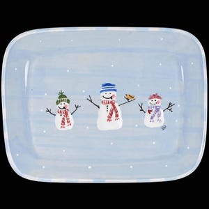 May include: A rectangular ceramic serving platter with a light blue background featuring a white painted border and small white dots. Three hand-painted snowmen are centered on the platter, each wearing a colorful hat and scarf, with a small bird.