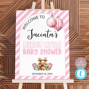 May include: A pink and white striped baby shower sign on an easel. The sign reads "Welcome to Jacinta's Merry Little Baby Shower" with a teddy bear and reindeer graphic. The date "December 16, 20XX" is also displayed.