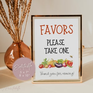 May include: A printable sign with the text "FAVORS PLEASE TAKE ONE" in black and red text. The sign features a watercolor illustration of various vegetables and a bee. The sign also includes the text "Thank you for coming!" in black text. The sign is framed in a gold frame and is sitting on a table.