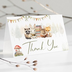 Peut inclure: Carte de remerciement pliée avec une illustration à l'aquarelle d'animaux de la forêt lisant des livres. Un raton laveur, un lapin, un hérisson et un renard sont représentés. La carte présente également un champignon sur une pile de livres et les mots "Thank You" en vert.