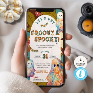 Może przedstawiać: Smartfon wyświetla zaproszenie na Halloween z tekstem "LET'S GET GROOVY & SPOOKY!" w stylu retro. Projekt zawiera kolorowe duchy, nietoperze i elementy kwiatowe. Zaproszenie zawiera szczegóły wydarzenia i informacje RSVP.