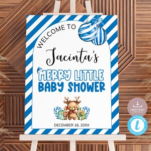 Puede incluir: Un letrero de baby shower sobre un caballete con un borde a rayas azules y blancas. El letrero dice "Bienvenida a Merry Little Baby Shower de Jacinta" con ilustraciones festivas de adornos, un reno y regalos. También se muestra la fecha "16 de diciembre de 20XX".