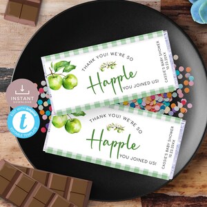 Op de afbeelding: Twee groene en witte chocolade-reepverpakkingen met een groen ruitjespatroon. De verpakkingen hebben een witte rand en tekst die luidt "Bedankt! We zijn zo blij dat je erbij was!" en "Cassie's Baby Shower 10.23.20XX". De verpakkingen bevatten een aquarelillustratie van groene appels aan een tak.
