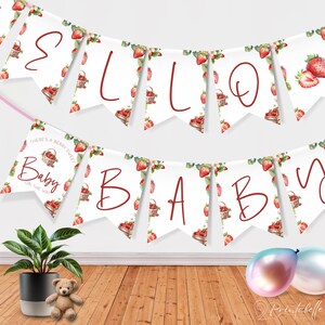 以下が含まれることがあります： 赤い筆記体で「Hello Baby」と「Baby」の文字が入った装飾バナー。水彩画のイチゴとバスケットで飾られています。「There's a berry sweet baby on the way」というフレーズも含まれています。鉢植え、テディベア、風船が前景にあります。
