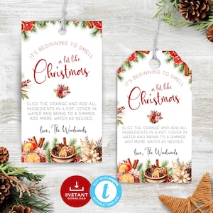 Op de afbeelding: Afdrukbare kerstcadeau-tag met een aquarel-illustratie van sinaasappels, kaneelstokjes, dennenappels en groen. De tekst luidt "It's beginning to smell a lot like Christmas. Slice the orange and add all ingredients in a pot. Cover in water and bring to a simmer. Add more water as needed. Love, The Woodwards."
