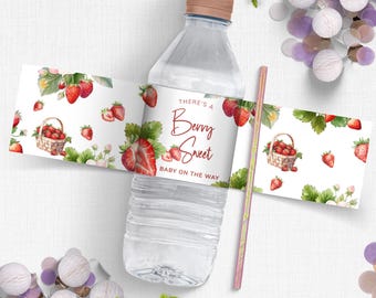 May include: A clear plastic water bottle with a brown cap and a decorative label. The label features a strawberry design with the text "There's a Berry Sweet Baby on the Way." A pink and yellow straw is next to the bottle.