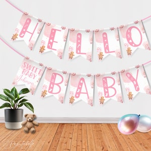 Op de afbeelding: Roze en witte baby shower banner met de woorden "Hello Sweet Baby Johnson" en illustraties van gingerbreadkoekjes.