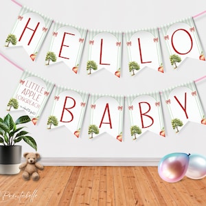 May include: A green and white banner with red letters that reads "Hello Baby". The banner has a red apple and green tree design. There is a smaller banner that reads "Little Apple Longreach is about to fall!"