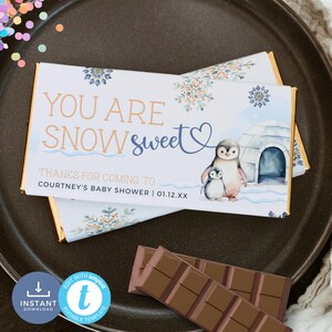 May include: A printable chocolate bar wrapper with a winter theme. It features a penguin family with a blue and white igloo in a snowy landscape. The text reads "You are snow sweet" and "Thanks for coming to Courtney's baby shower | 01.12.XX".