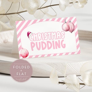 May include: A folded Christmas Pudding card with a pink and white striped border. The card features the words "Christmas Pudding" in pink, along with illustrations of ornaments and a Santa hat. The card is designed to be folded or laid flat.