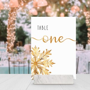 Image of a Table Number sitting in a wooden slotted holder on a light-colored wooden bench with outdoor dinner party scene in background.