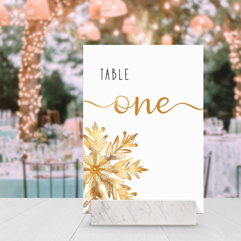 Image of a Table Number sitting in a wooden slotted holder on a light-colored wooden bench with outdoor dinner party scene in background.