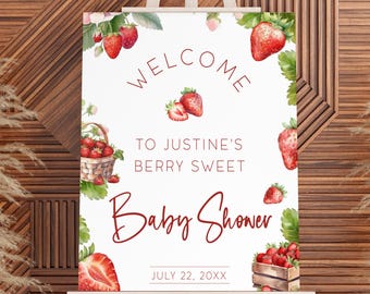 May include: A white welcome sign on an easel with a strawberry theme. The sign reads "Welcome to Justine's Berry Sweet Baby Shower" with watercolor strawberries and greenery. The date July 22, 20XX is also displayed.